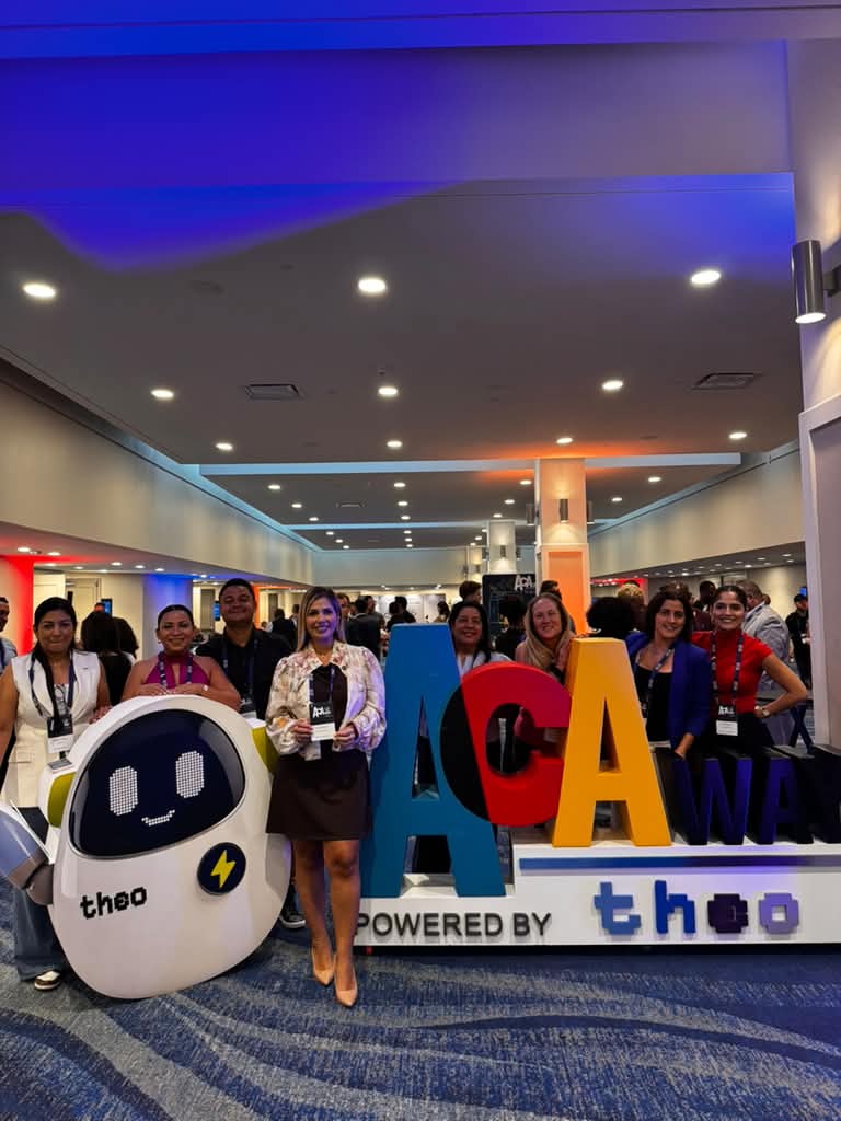 Grupo amplio de asistentes posa junto a las letras de ACA Way y la mascota del evento.